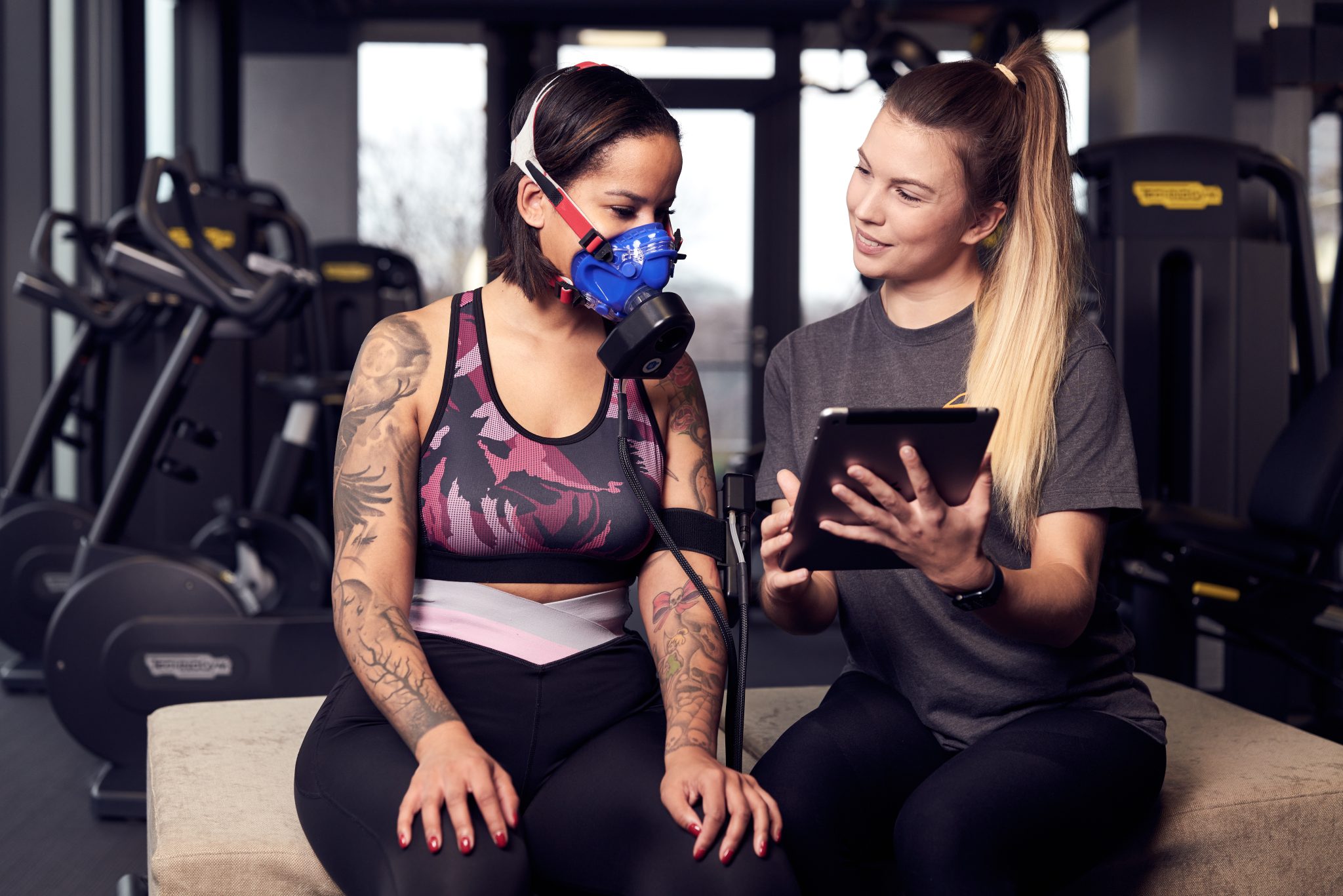 Zwei Frauen in einem Fitnessstudio schauen auf ein Tablet.