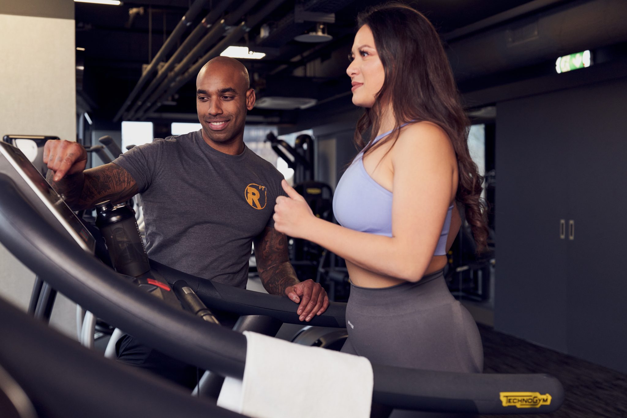 Ein Mann und eine Frau unterhalten sich auf einem Laufbandgerät in einem Fitnessstudio.